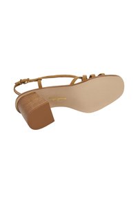 Sandale à talon beige avec un design à brides, présentant un talon bloc texturé et une semelle extérieure lisse. Marque dorée visible sur la semelle intérieure.