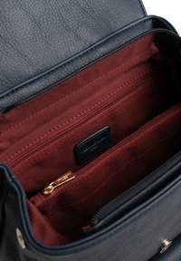 Skórzana torba w kolorze granatowym z fakturowanym wykończeniem. Wnętrze podszyte czerwonym materiałem, wyposażone w zasuwane kieszenie z elementami w kolorze złotym.