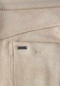 Tissu en suède beige avec des détails de couture visibles et une petite étiquette métallique rectangulaire portant l'inscription "Street One."