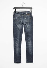 Mörkblå smala jeans hängande på en galge. Har fem fickor, synlig sömnad och lätta blekningar. Äkta denimmaterial.