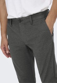 Pantalones con patrón de espiga en gris, de textura suave, con cierre de botón y bolsillos laterales, que presentan un ajuste entallado.