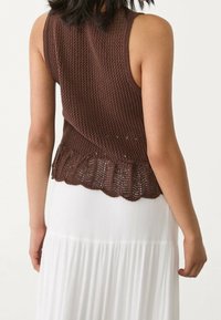 Brązowy dzianinowy top bez rękawów z teksturowanym wzorem i falbankowym dołem, zestawiony z lejącą się białą spódnicą z pionowymi plisami.