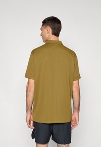 Olivenfarget polo skjorte med korte ermer, enkel design, myk tekstur og rett hem. Brukt med mørke shorts. Bakside.