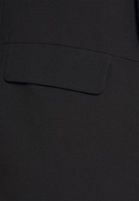 Černá ušitá látka s hladkou texturou, na přední straně s jednou čtvercovou kapsou.