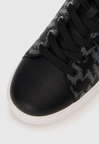 Black synthetic sneaker with textured leather finish, glossy houndstooth pattern, flat black laces, and white rubber sole.