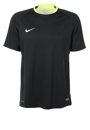 Homme portant une tenue de sport noire et jaune néon, un short noir à motifs, des chaussettes noires montant jusqu'aux genoux et des chaussures noires avec des lacets verts néon.