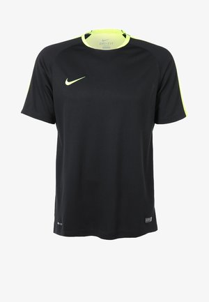 Mann trägt schwarze und neongelbe Sportkleidung, schwarze gemusterte Shorts, kniehohe schwarze Socken und schwarze Schuhe mit neongrünen Schnürsenkeln.