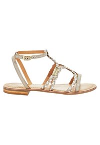 Sandali pianeggianti realizzati in pelle grigia chiara, con cinturini incrociati con dettagli metallici e chiusura a fibbia. Sole in legno liscio.