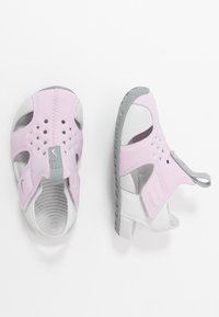 Sandali rosa e bianchi con design aperto, realizzati in materiale flessibile. Presentano perforazioni, una fascia grigia e una suola testurizzata per una buona aderenza.