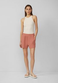 Weißes geripptes Tanktop kombiniert mit ziegel farbigen strukturierten Shorts mit einem elastischen Bund. Sandalen mit weißen Riemen runden das Outfit ab.