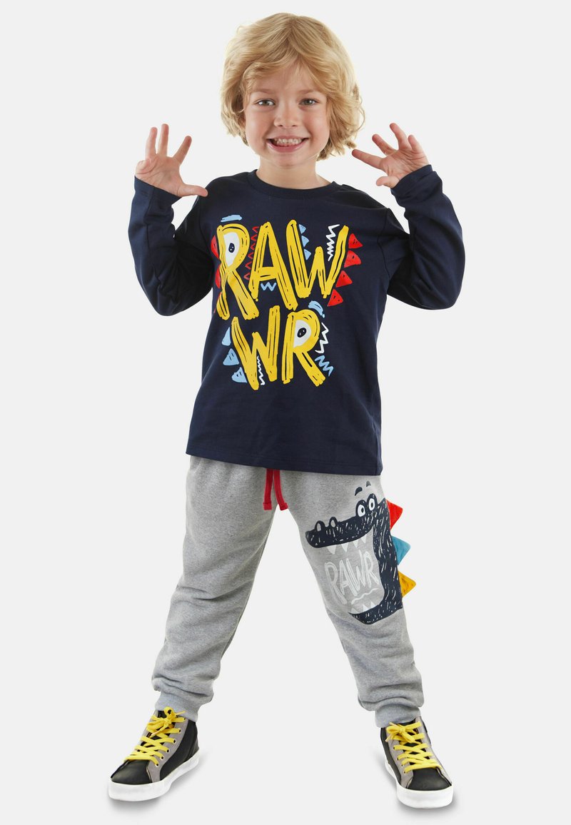 Marineblaues Langarmshirt mit buntem "RAWR"-Grafik, kombiniert mit grauen Jogginghosen mit Dinosaurierdesign, rotem Kordelzug und schwarzen Sneakern.
