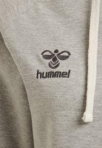 Sudadera gris con tejido texturizado, cordones de color natural y un logotipo bordado en negro en la zona del pecho.