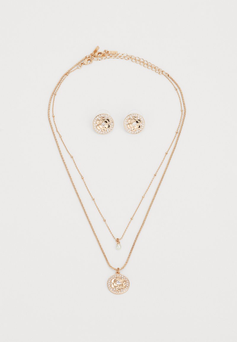 Arany színű ékszerszett, amely egy rétegelt nyakláncból áll, kör alakú medállal, és illeszkedő, virágmintákkal és díszítésekkel díszített kerek fülbevalókból.