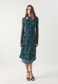 Teal kukkakuosi mekko, jossa on pitkät läpikuultavat hihat, epäsymmetrinen helma ja kiertyvä kaula-aukko. Kangas on pehmeä ja kevyt.