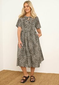 Sukienka w panterkę z krótkimi rękawami, dekoltem w kształcie łezki, dopasowaną talią i zwiewnym dołem. Noszona z brązowymi sandałami z ćwiekami na teksturowanej macie.