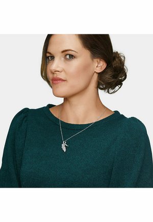 Silberne Halskette mit Blatt-Anhänger, getragen von einer Person in einem strukturierten türkisfarbenen Pullover. Der Anhänger verfügt über filigrane Details, die sein Design unterstreichen.