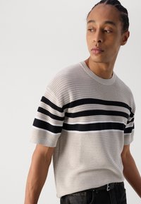 Strickpullover mit kurzen Ärmeln in Beige, der horizontale Streifen in Marineblau und Weiß aufweist. Rundhalsausschnitt, strukturiertes Gewebe und lockere Passform.