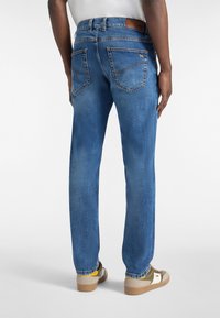 Jeans de mezclilla azul con corte recto, dos bolsillos traseros con costuras naranjas y un parche de cuero marrón en la cintura.