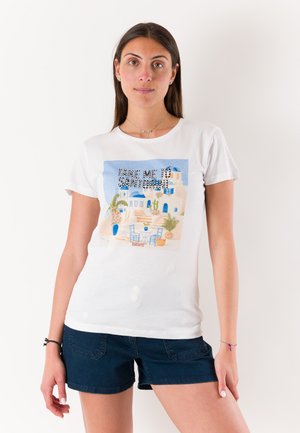 Donna con maglietta bianca con illustrazione di Santorini e testo "Portami a Santorini", abbinata a pantaloncini blu scuro su sfondo semplice.