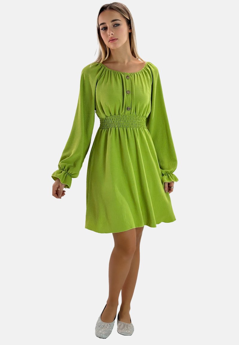 Vestido verde con mangas largas, cintura fruncida y detalles de botones. Textura suave y falda acampanada, combinado con bailarinas plateadas brillantes.