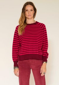 Pull en maille rayé magenta et bordeaux à manches longues et à ourlet côtelé, associé à un pantalon en velours côtelé assorti. Texture lisse.