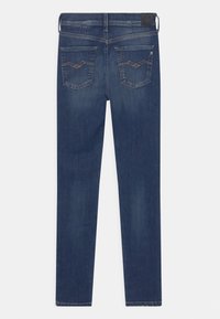 Jeans de ganga azul escuro com um corte slim. Apresenta dois bolsos traseiros com costura decorativa e uma etiqueta de couro na cintura.