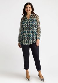 Przezroczysta bluzka z długim rękawem w kwiatowy wzór w odcieniach niebieskiego i zielonego, z kołnierzykiem i zapięciem na guziki, zestawiona z ciemnymi spodniami.
