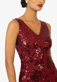 Abito bordeaux con scollatura a V, ricamo floreale in paillettes e maniche a canottiera. Tessuto morbido con silhouette aderente. Orecchini argento visibili.