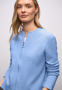 Jasnoniebieski sweter na zamek wykonany z miękkiego dzianinowego materiału, z okrągłym dekoltem i ściągaczami o subtelnej fakturze.