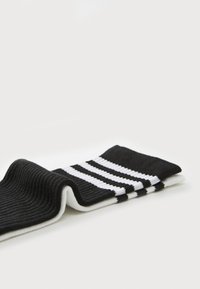Meias caneladas em preto e branco com três riscas horizontais brancas, dobradas sobre uma superfície branca.