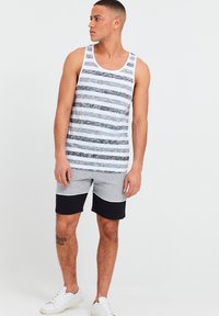 Stripet tanktop i grå og hvid med vandrette linjer; grå og sorte shorts med farveblokke; hvide sneakers.
