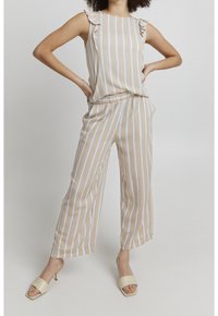 Tuta leggera con spalline a volant, strisce verticali beige e bianche, vita elastica e pantaloni a gamba larga. Abbinate a ciabatte beige.