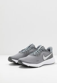 Šedé sportovní boty s mesh svrškem, se bílou mezipodešví, šedými akcenty a designem zaoblené špičky. Výrazné logo Nike na boku.