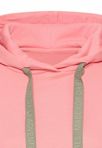 Roze pullover hoodie met een zachte textuur, voorzien van een dubbel gelaagde capuchon en lichtgroene trekkoorden met het label "MADE FOR DAILY ADVENTURES."