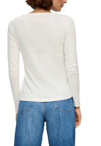 Langärmelig top van zachte witte katoen met een ronde halslijn en een rechte pasvorm, gecombineerd met lichtblauwe high-waisted denim jeans.