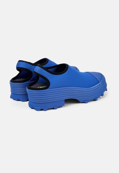 Blå gummistövlar i slip-on-modell med texturerad sula, dragtab vid hälen och svart kant runt öppningen, med ett räfflat mönster.