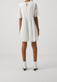 Vestido blanco de volantes con mangas cortas, patrón de lunares texturizados, detalle de escote en forma de llavero en la parte trasera, combinado con botas blancas hasta el tobillo.