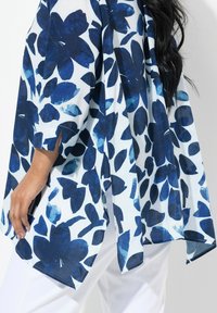Blusa a fiori blu e bianchi con una vestibilità morbida, maniche corte con aperture e un orlo curvo. Tessuto leggero e trasparente.
