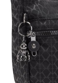 Black textured backpack featuring a geometric pattern, a silver monkey keychain, and a zippered pocket with a branded pull tab.