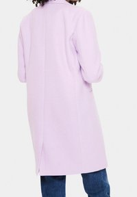 Cappotto in misto lana lilla con maniche lunghe, uno spacco posteriore e design su misura. Il tessuto ha una superficie liscia e uno stile minimalista.