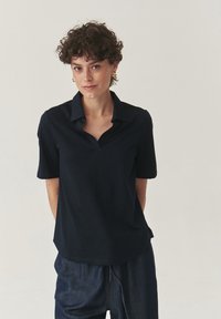 Camicia blu navy a maniche corte con design a collo a V, realizzata in tessuto morbido. Abbinata a pantaloni larghi in denim scuro.
