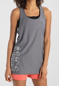 Canotta sportiva grigia senza maniche con finitura strutturata e logo riflettente "ASICS" sul lato, abbinata a pantaloncini rosa.