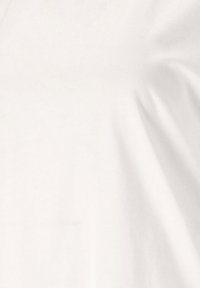 Valkoinen puuvillapaita, lyhyet hihat, sileä pinta, yksinkertainen muotoilu, jossa on hieman roikkumista, joka luo pehmeitä poimuja. Ei näkyviä kuvioita tai koristeita.