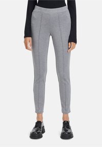 Šedé legíny vyrobené z měkkého materiálu, s přiléhavým střihem, vertikálními švy a elastickým pasem, v kombinaci s černými robustními botami.