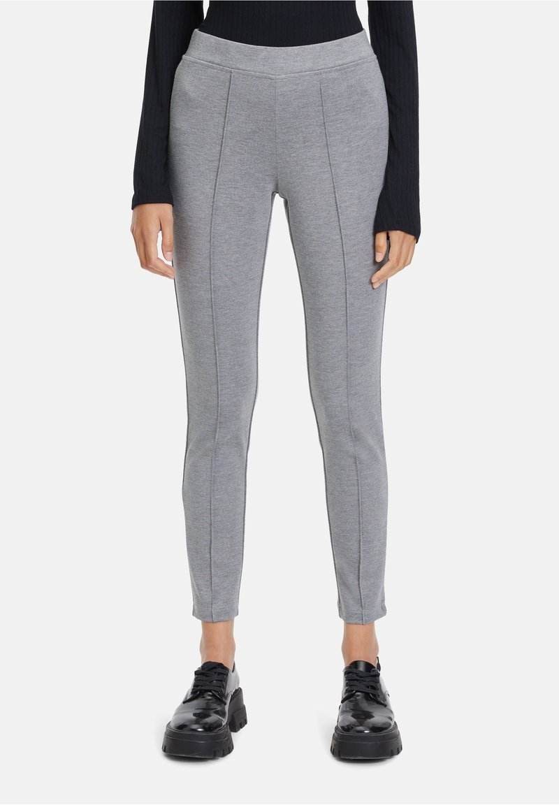 Šedé legíny vyrobené z měkkého materiálu, s přiléhavým střihem, vertikálními švy a elastickým pasem, v kombinaci s černými robustními botami.