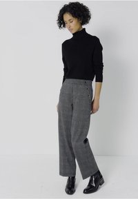 Svart polotröja i kombination med grå rutig hög-midja byxor med sidoknappar. Modellen har på sig svarta ankelstövlar.