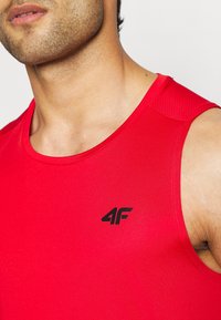Gros plan d'une personne portant un débardeur de sport rouge avec un logo 4F noir sur la poitrine.