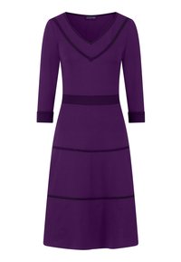 Valkoinen mekko, jossa on V-kainalo, kolmanneksen hihat ja mustat korostusviivat tiukassa muotoilussa, valmistettu pehmeästä ja joustavasta materiaalista.