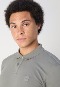 Polo shirt in lichtgrijs, gemaakt van een gestructureerde katoenmix, met een tweeknops sluiting, kraag en een klein merklabel op de borst.