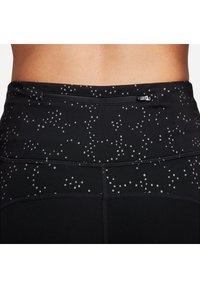 Svarta träningstights med passformande design, prydda med ett prickigt mönster i ljusgrått och en säker dragkedjeficka bak.